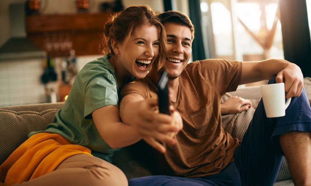 Fröhliches Paar sitzt mit Fernbedienung auf dem Sofa